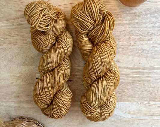 Two skeins of camel colored hand dyed wool yarn against a wood background.