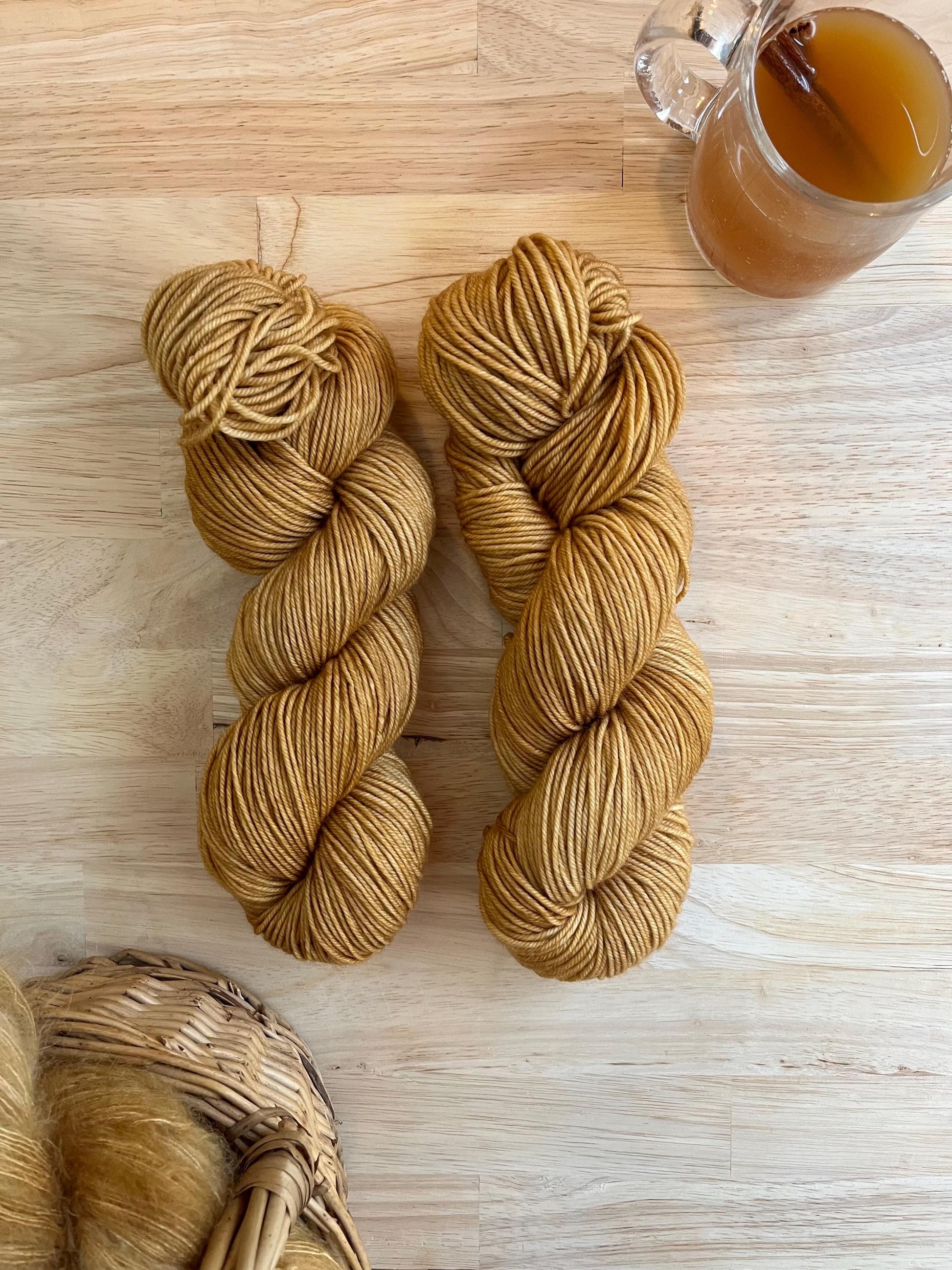 Two skeins of camel colored hand dyed wool yarn against a wood background.