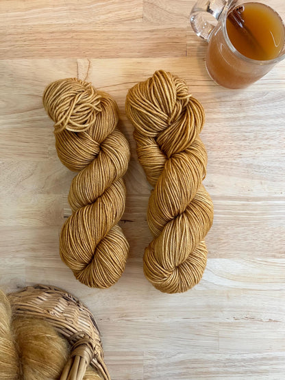 Two skeins of camel colored hand dyed wool yarn against a wood background.