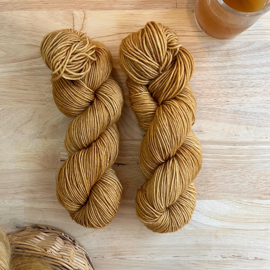 Two skeins of camel colored hand dyed wool yarn against a wood background.