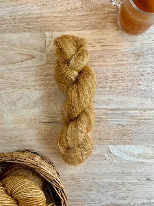 A skein of hand dyed golden camel colored mohair silk lace yarn, arranged against a wooden background.