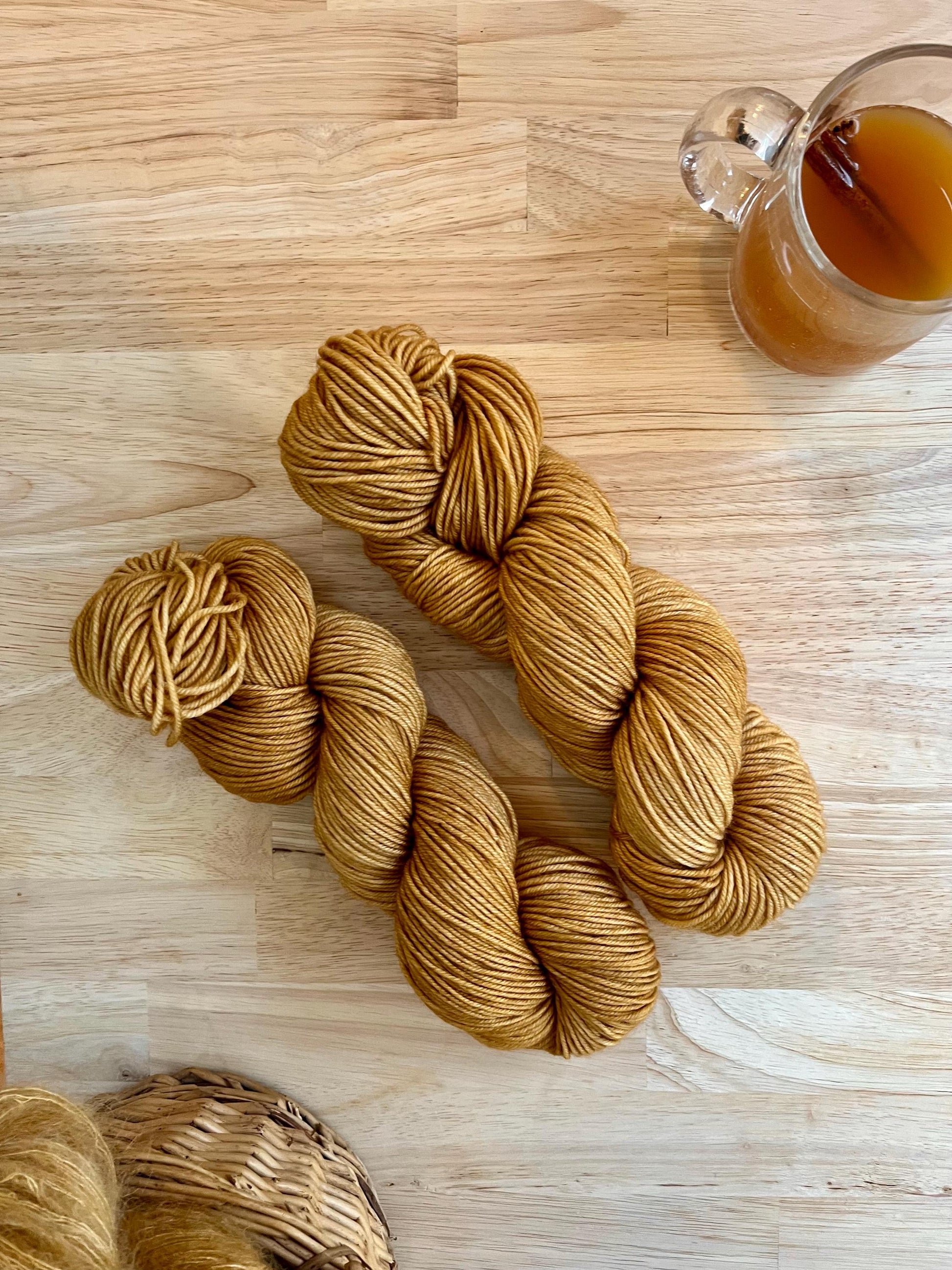Two skeins of golden tan colored hand dyed wool yarn against a wood background.