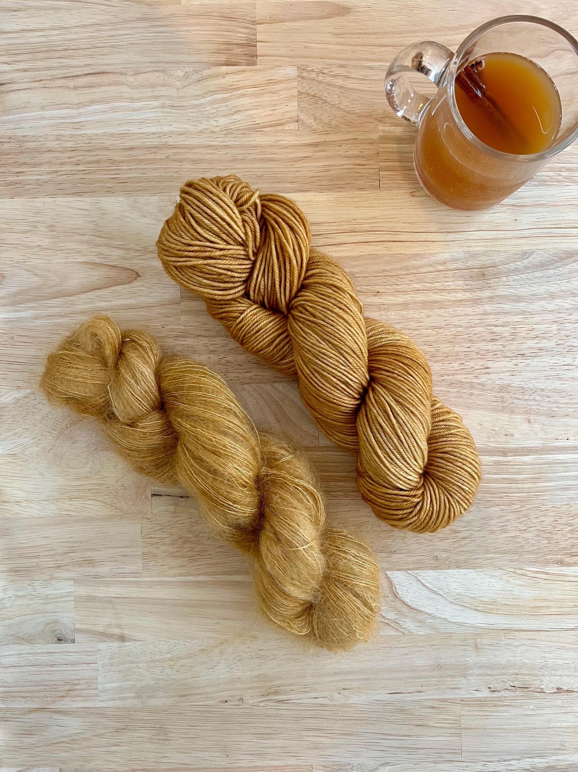 Two skeins of camel colored hand dyed wool yarn against a wood background. One skein is DK weight merino wool and the other is lace weight mohair and silk.