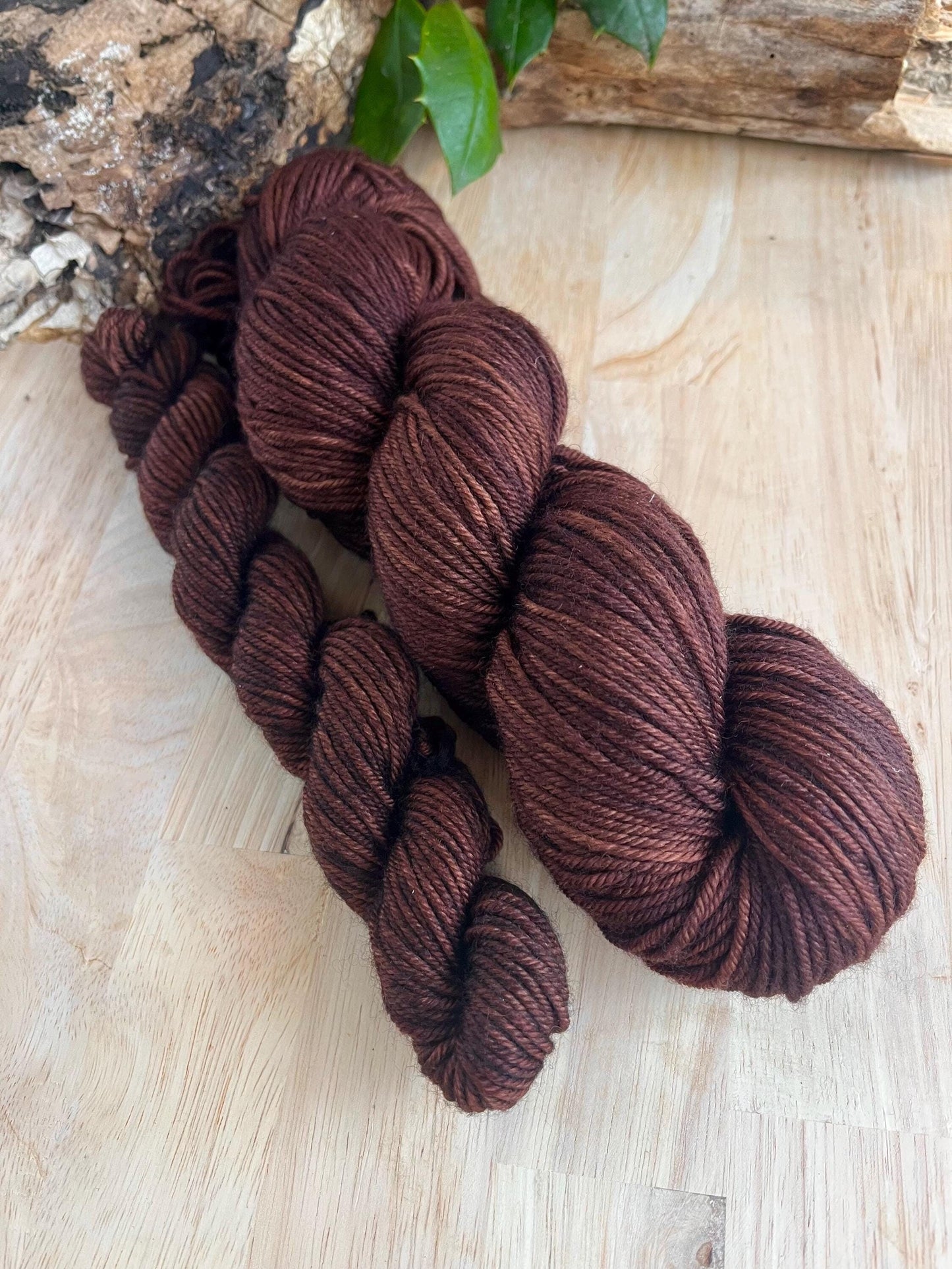 A mini skein and full size skein of dark brown hand dyed merino wool yarn