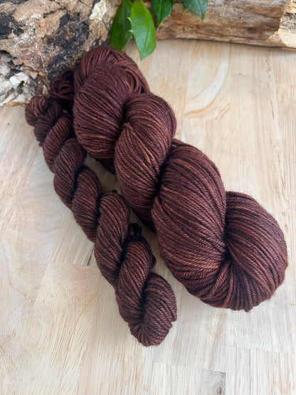 A mini skein and full size skein of dark brown hand dyed merino wool yarn