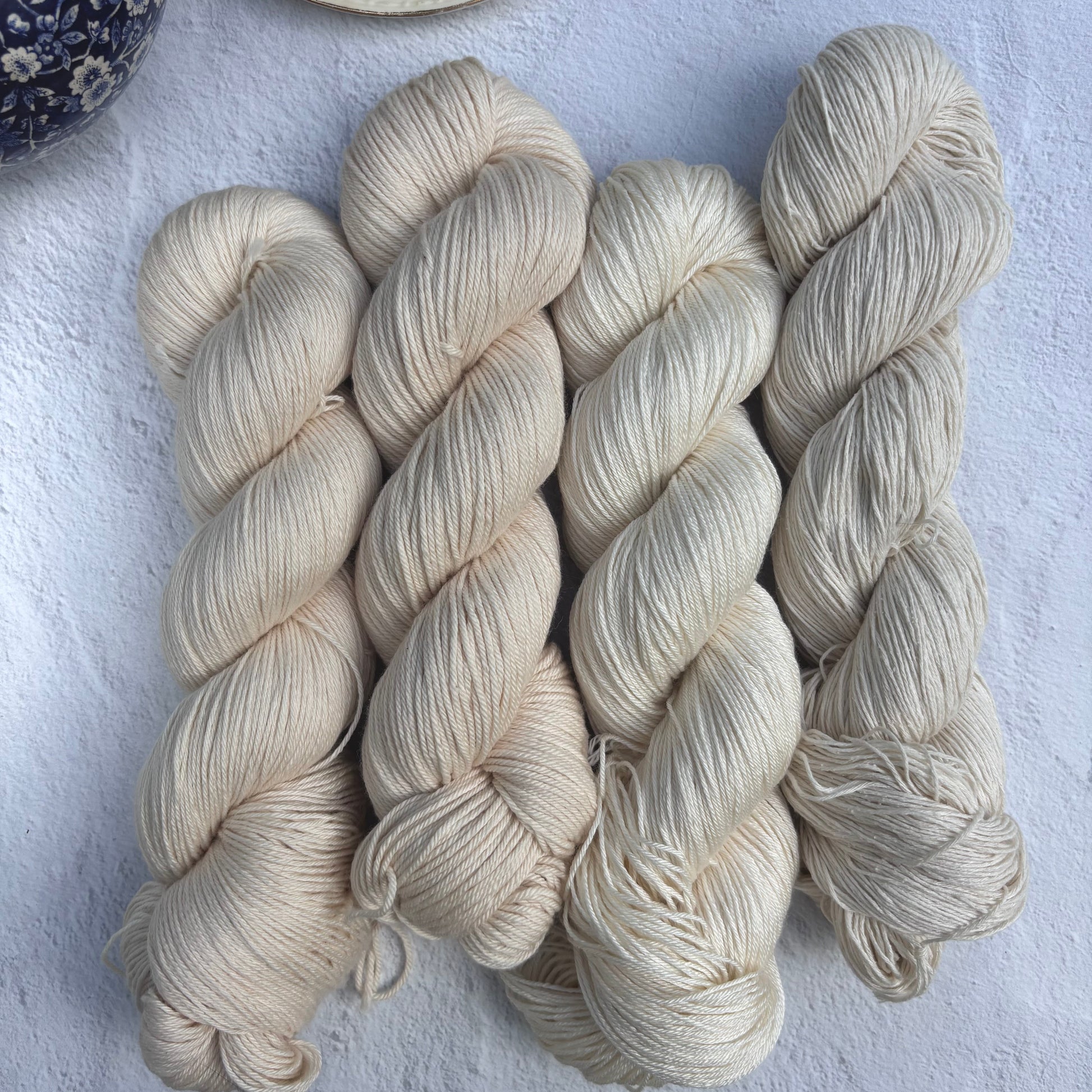 Skeins of cream-colored yarn on a light blue surface with a cup and saucer in the background.