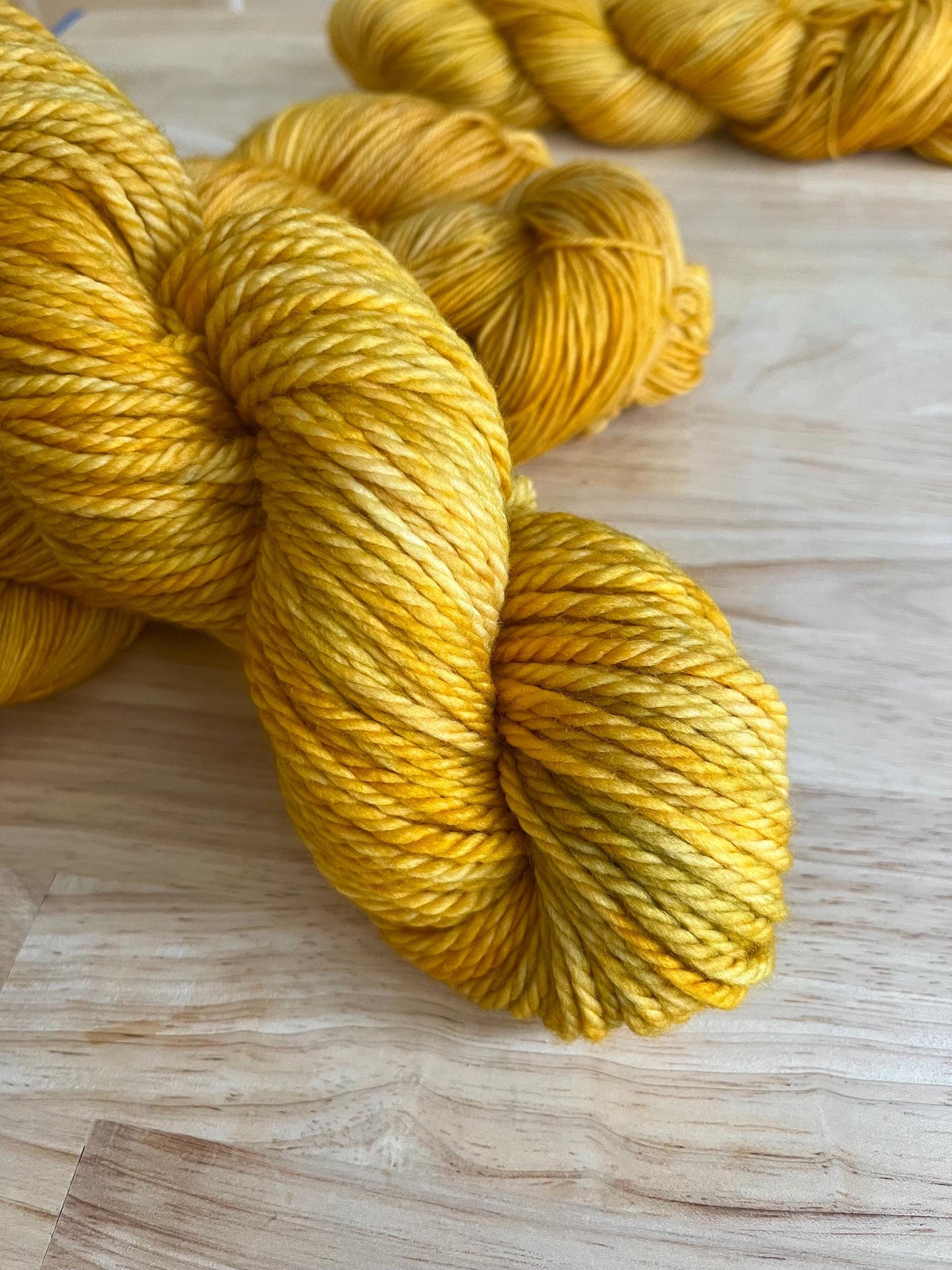 A skein of bulky weight hand dyed variegated yellow and gold wool yarn.