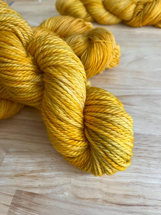 A skein of bulky weight hand dyed variegated yellow and gold wool yarn.