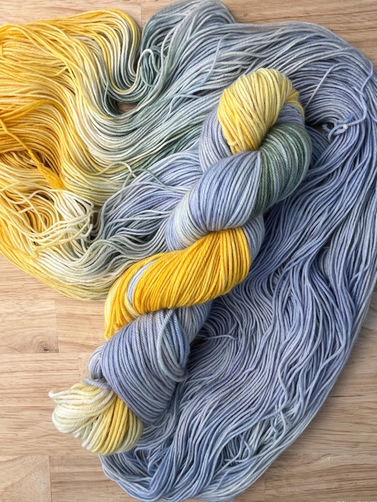 A skein of pale blue and yellow hand dyed merino wool yarn designed for assigned pooling.