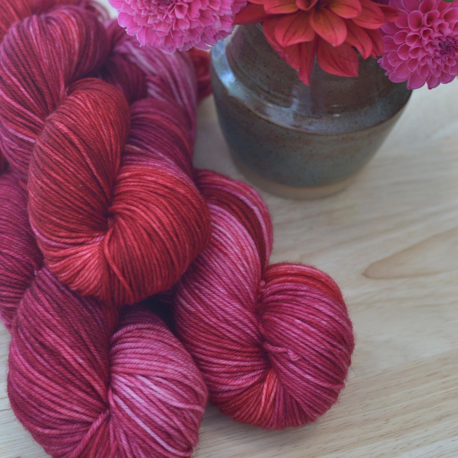 Skeins of pink and red hand dye merino wool yarn arranged with flowers.
