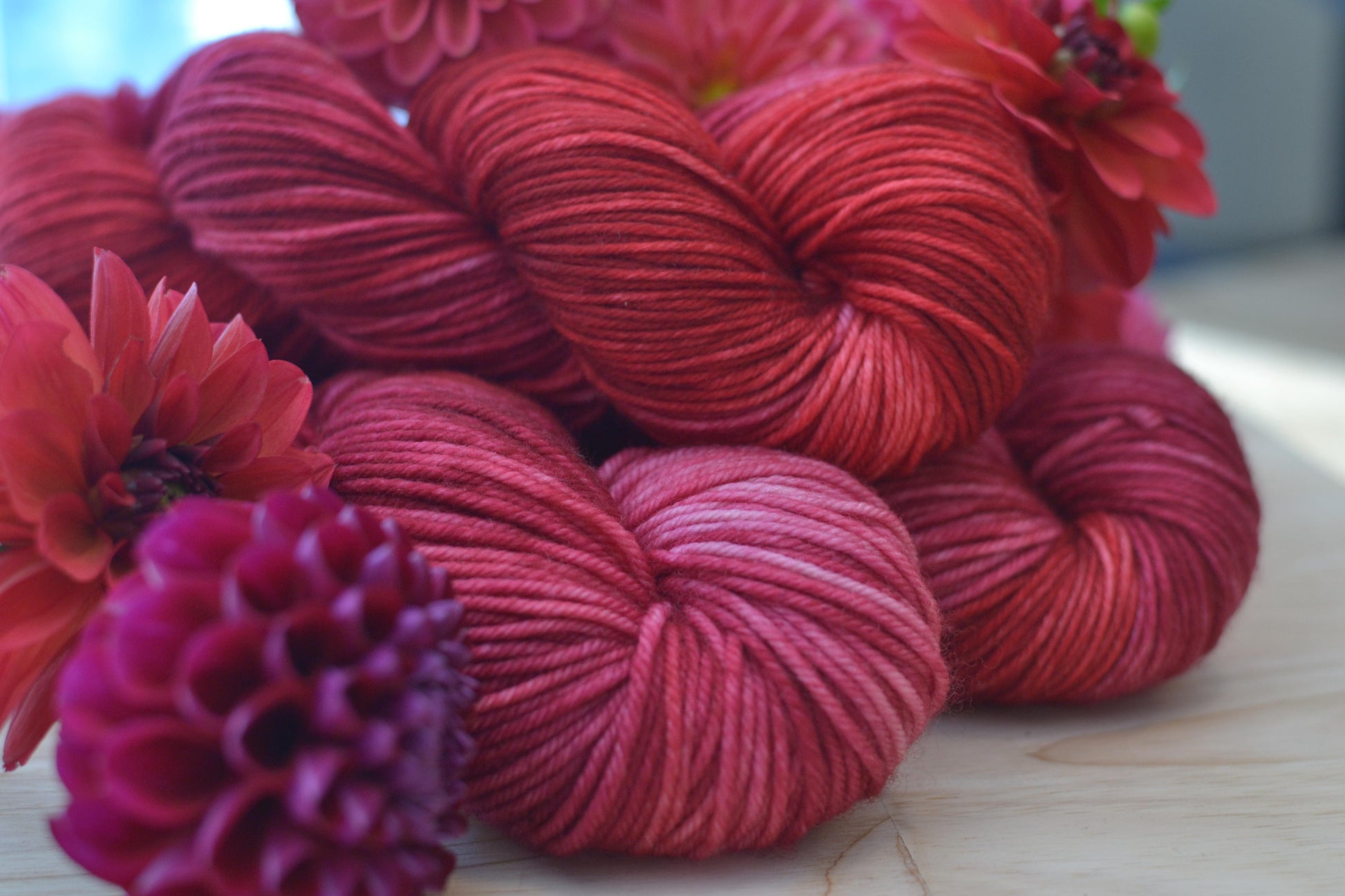 Skeins of pink and red hand dye merino wool yarn arranged with flowers.