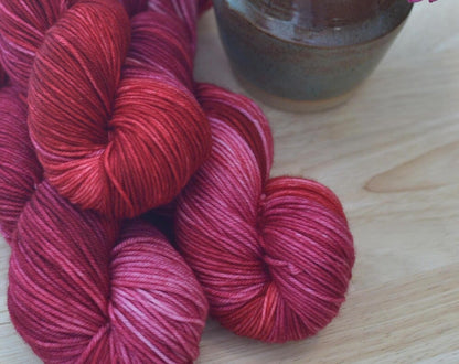 Skeins of pink and red hand dye merino wool yarn arranged with flowers.