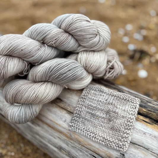 Gray skein of yarn and knitted fabric on a wooden surface with a blurred natural background