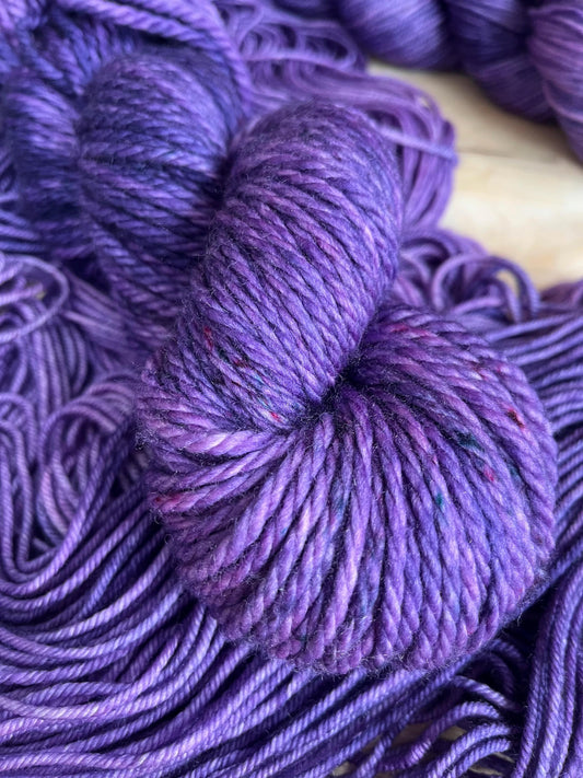 A skein of bulky weight hand dyed speckled tonal purple merino wool yarn