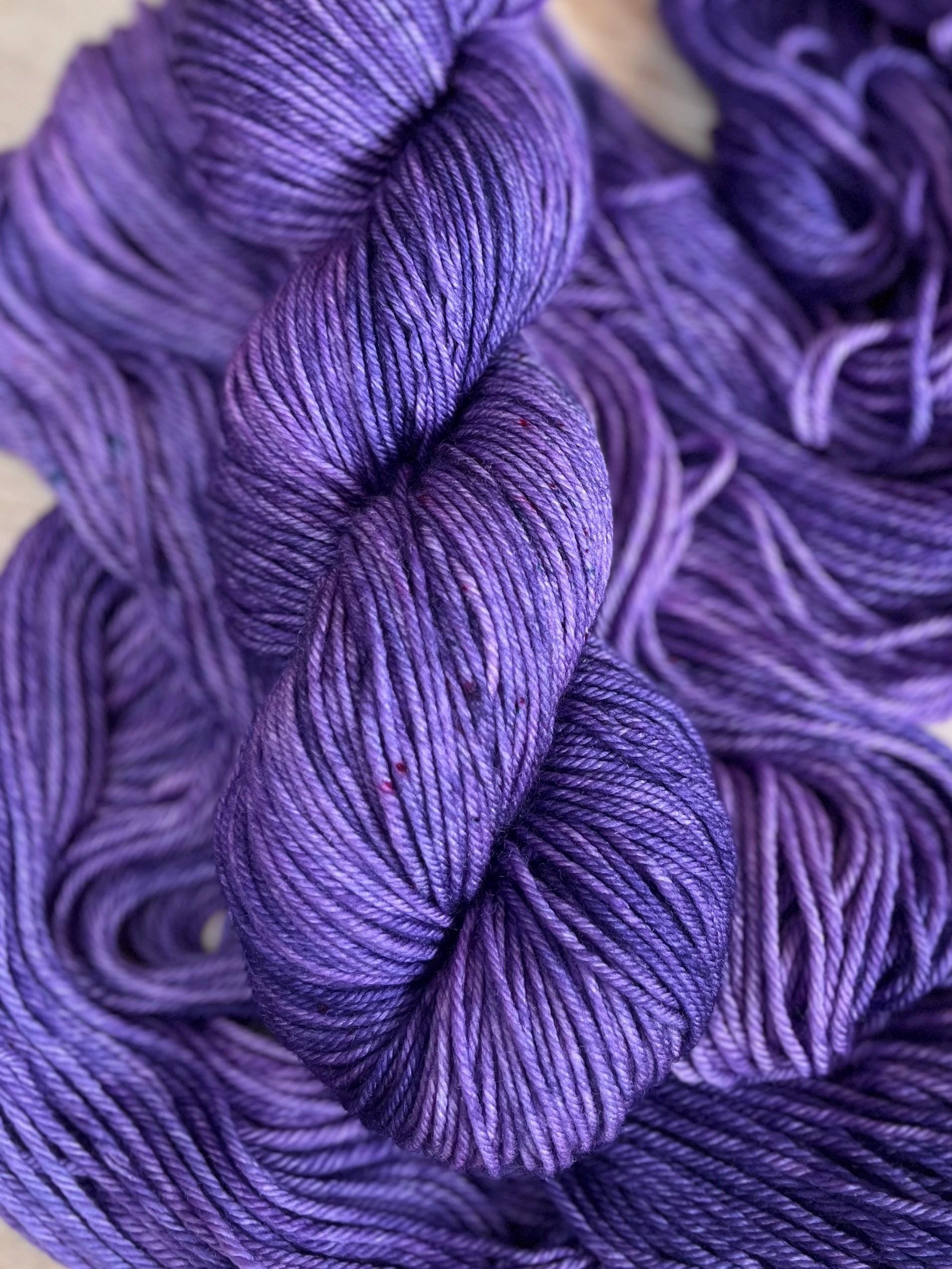 A skein of DK weight hand dyed speckled tonal purple merino wool yarn