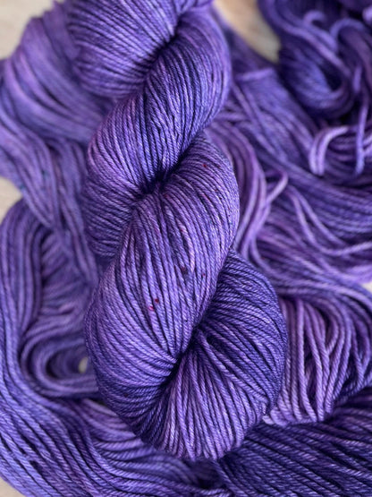 A skein of DK weight hand dyed speckled tonal purple merino wool yarn