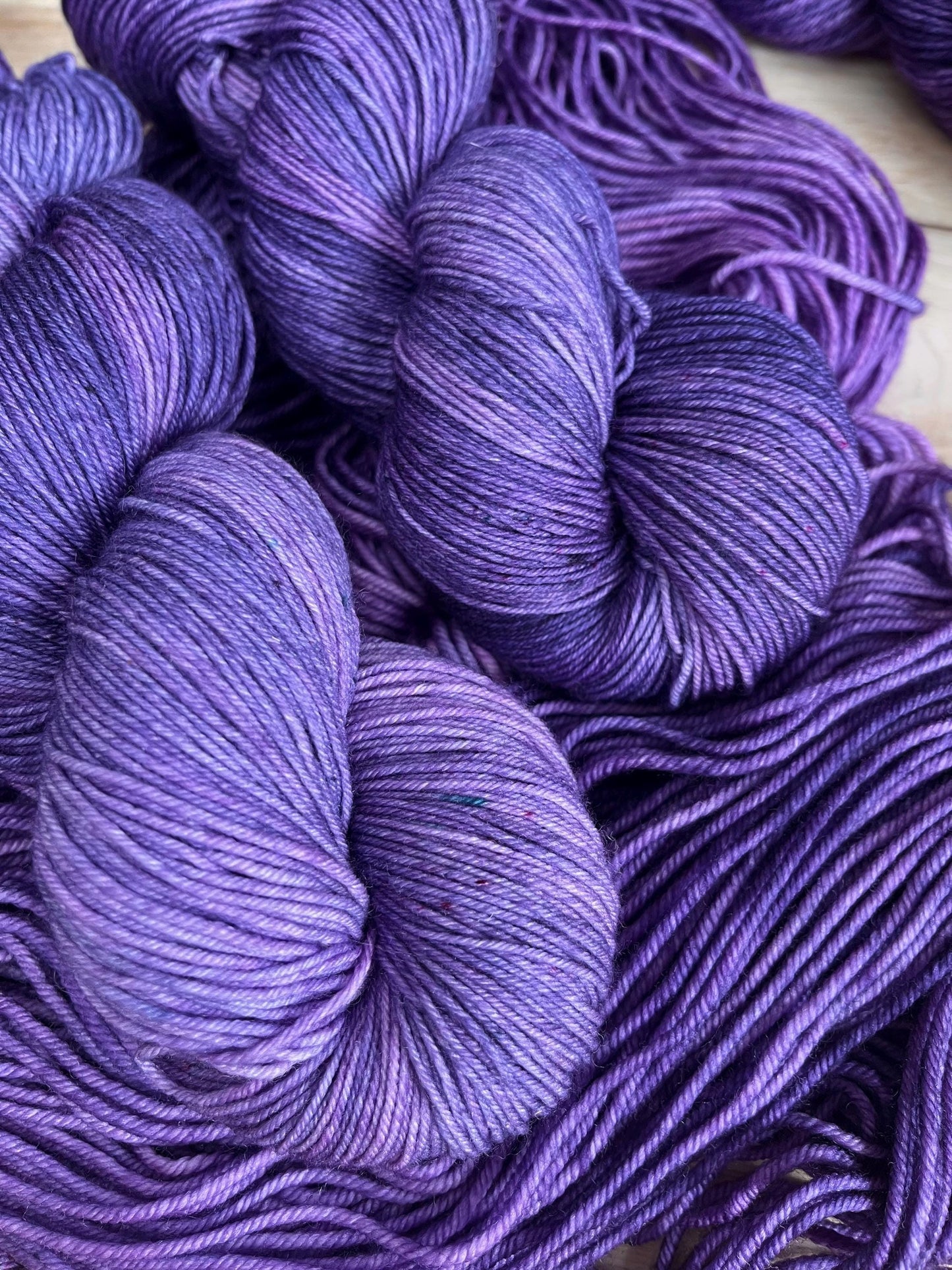 Skeins of sock weight hand dyed speckled tonal purple merino wool yarn