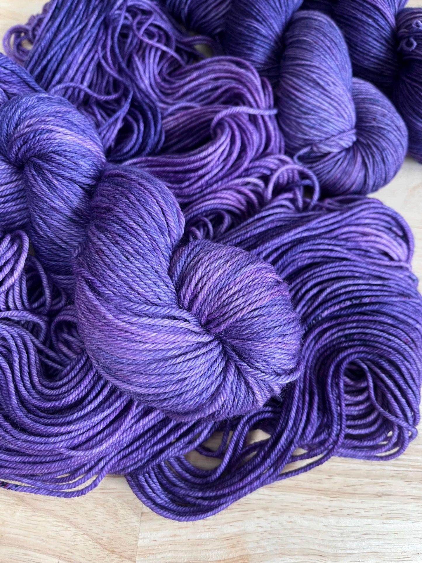 A skein of worsted weight hand dyed speckled tonal purple merino wool yarn
