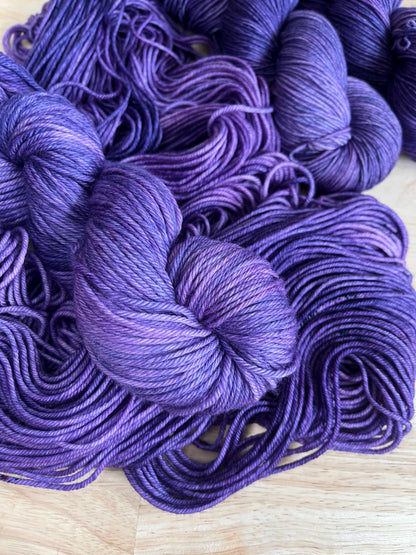 A skein of worsted weight hand dyed speckled tonal purple merino wool yarn