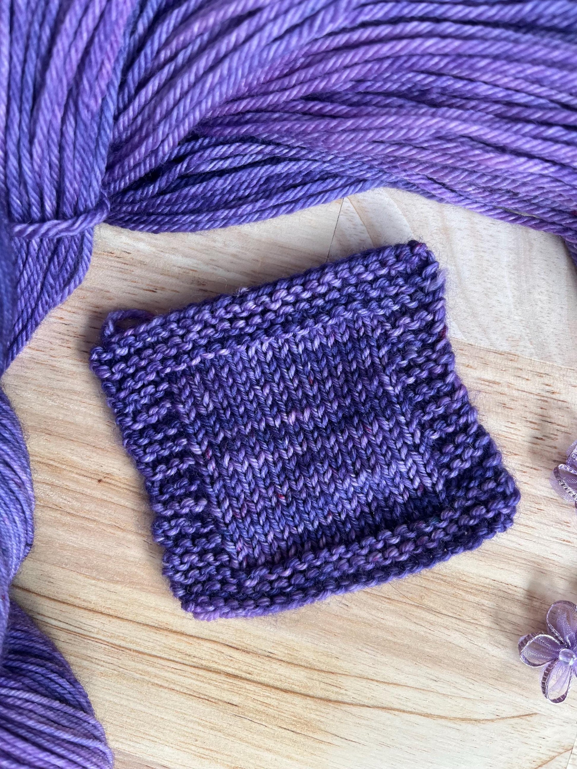 A knit swatch of hand dyed speckled tonal purple merino wool yarn