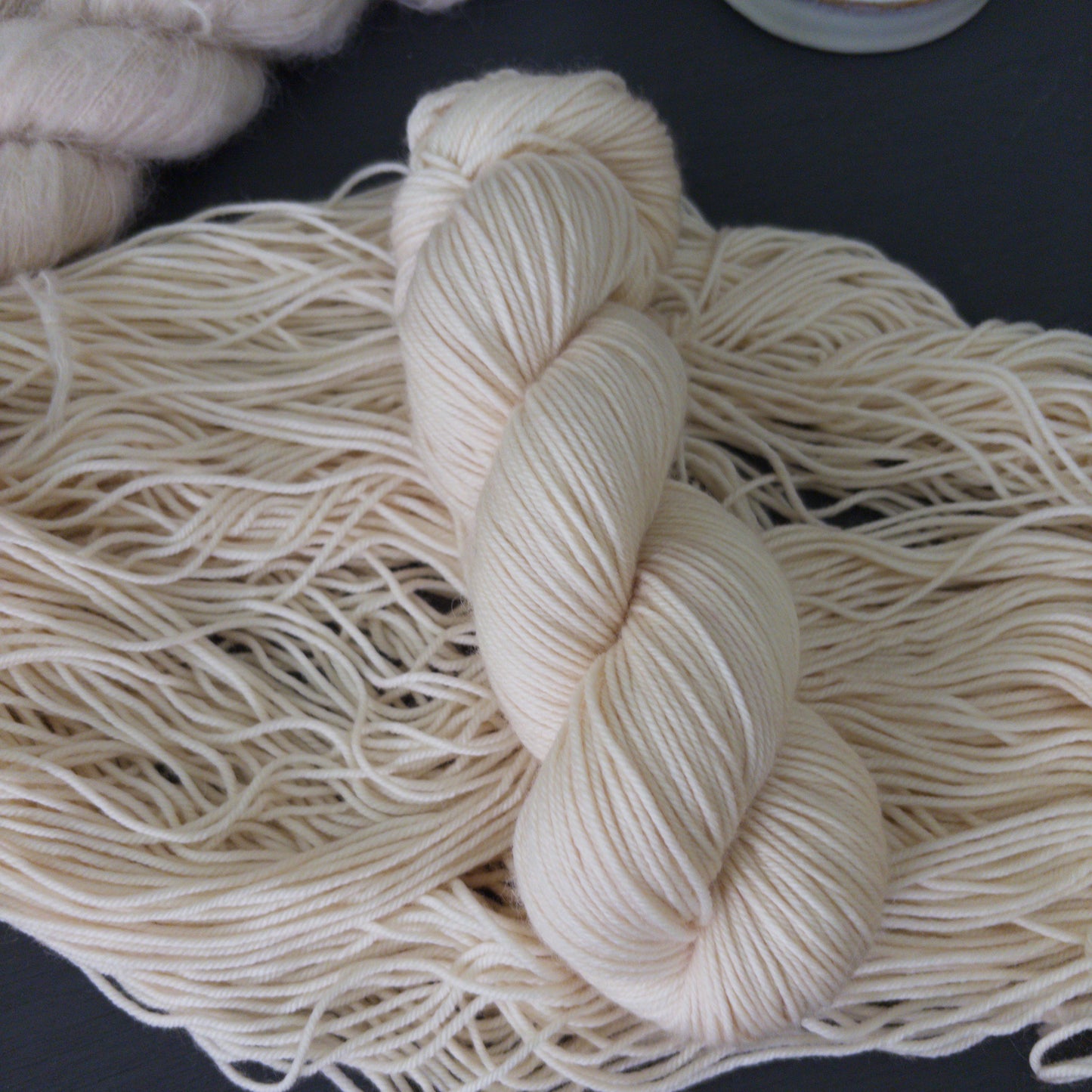 Close-up of skeins of hand dyed white wool yarn on a dark surface