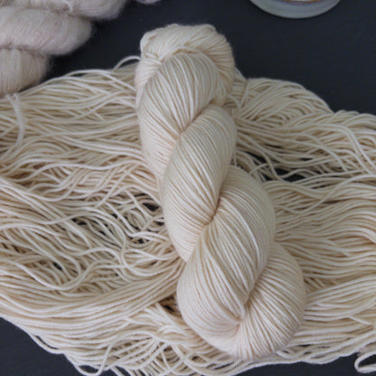 Close-up of skeins of hand dyed white wool yarn on a dark surface