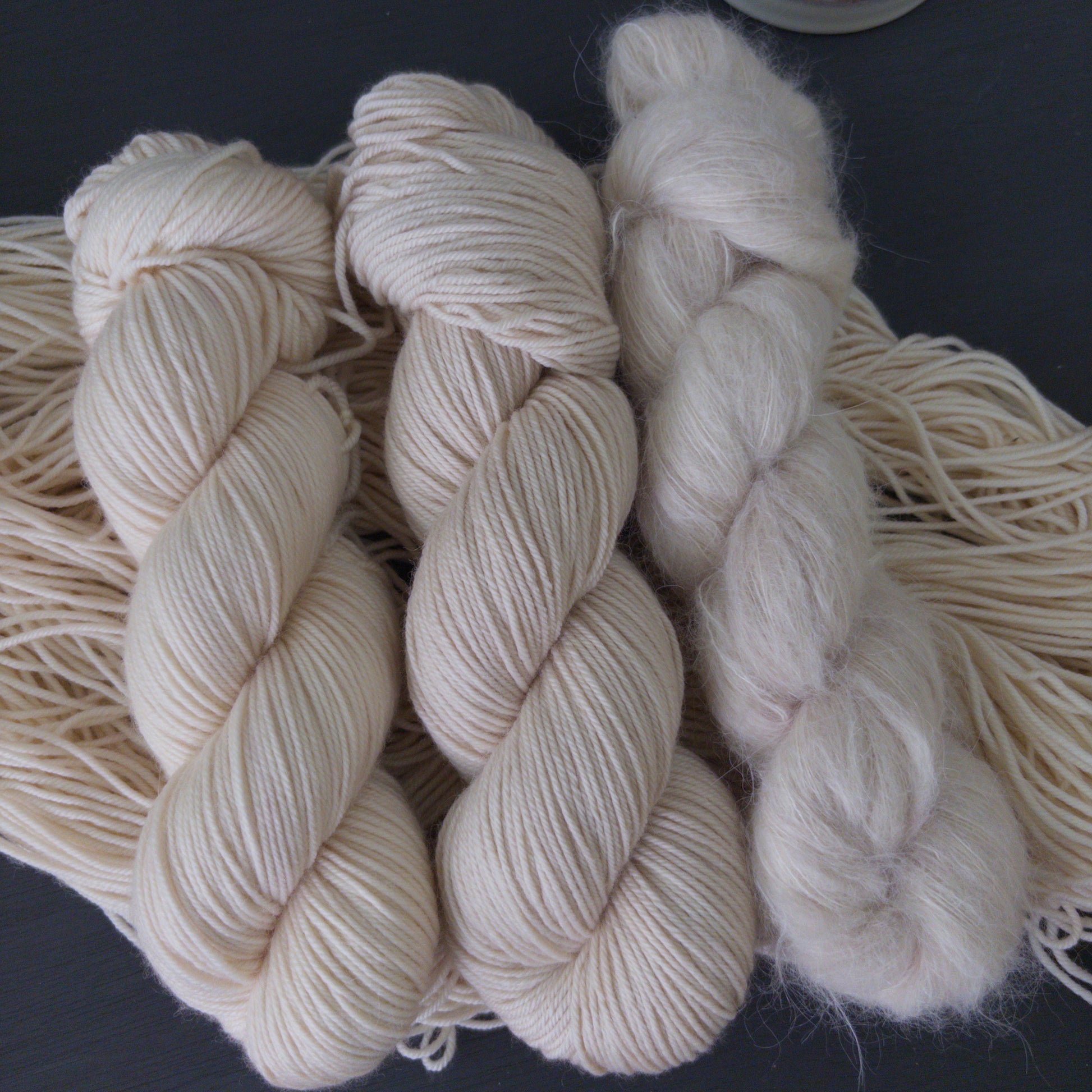Three skeins of cream-colored yarn on a dark surface with a white candlestick in the background.