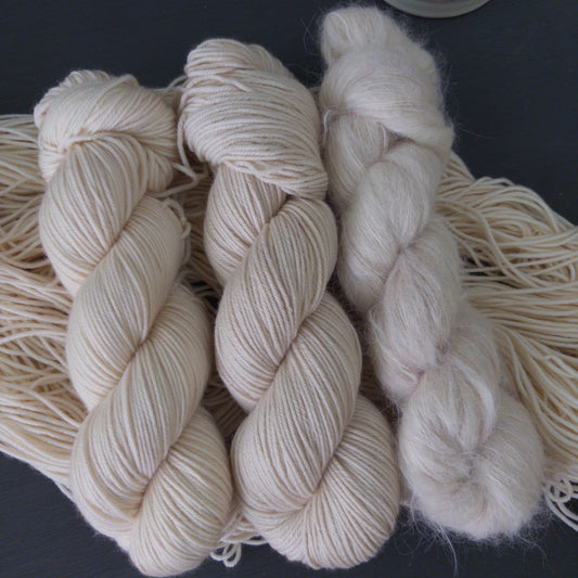 Three skeins of cream-colored yarn on a dark surface with a white candlestick in the background.