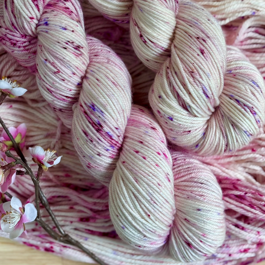 Two skeins of pink and white speckled yarn against a wood backdrop with a sprig of flowers