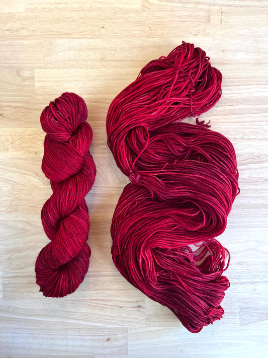 Two skeins of hand dyed red merino wool yarn arranged on a wood background.