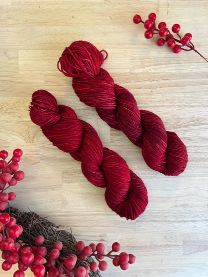 Two skeins of hand dyed red merino wool yarn arranged on a wood background.