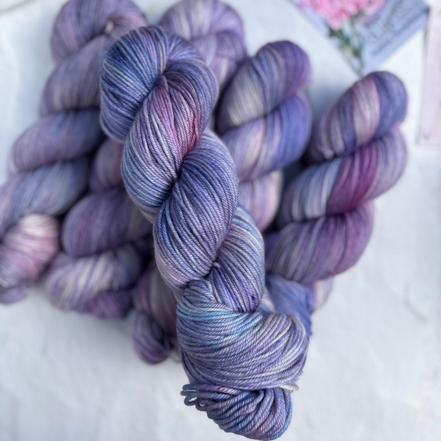 Purple and blue yarn skeins on a white surface with a floral card in the background