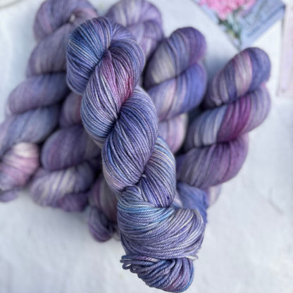 Purple and blue yarn skeins on a white surface with a floral card in the background