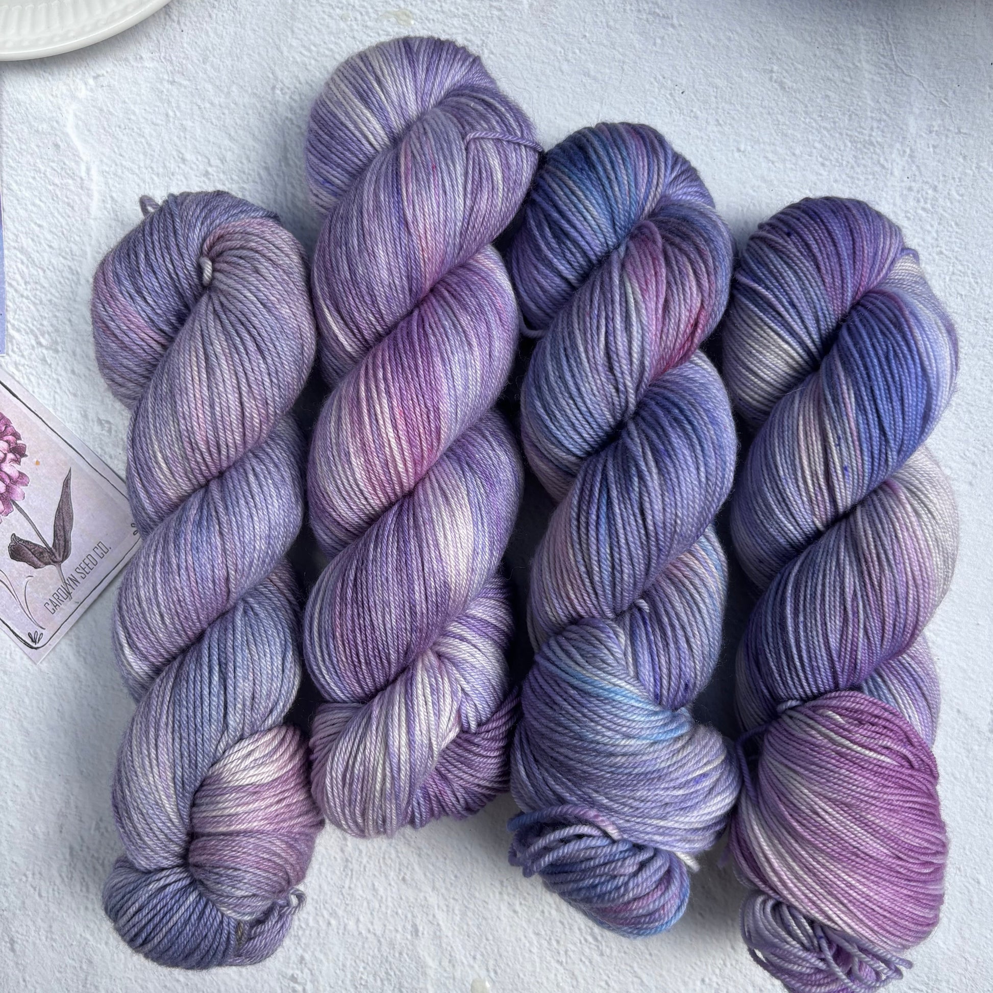 Four skeins of purple and blue yarn on a light gray surface.
