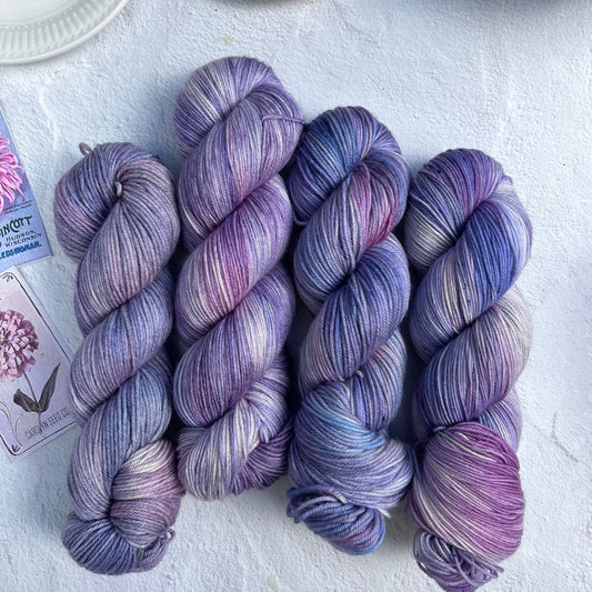Four skeins of purple yarn on a light surface with a teacup and saucer in the background.