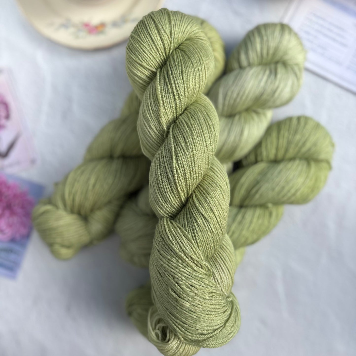 Green skein of yarn on a white surface with a cup and lemon in the background
