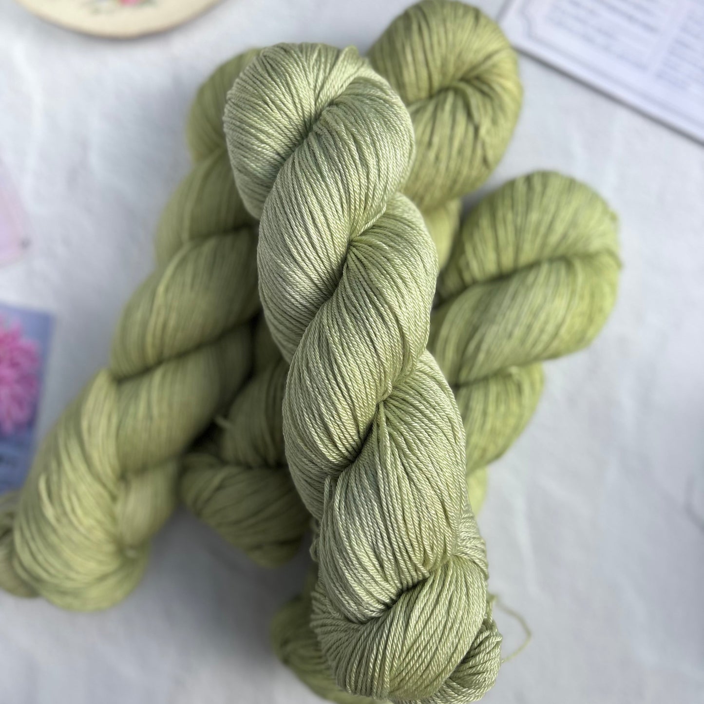 Skeins of green yarn on a light surface with a cup and saucer in the background.