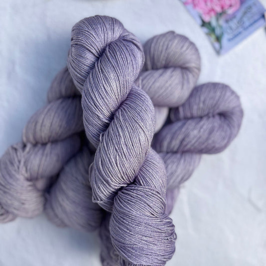 Bundles of purple yarn on a light gray surface with a decorative plate and fabric in the background.