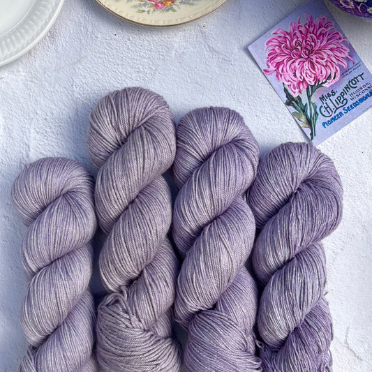 Four skeins of purple yarn on a white surface with a floral card in the background.