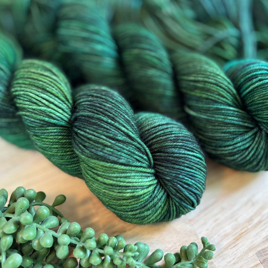 Green skeins of yarn on a wooden surface with greenery.