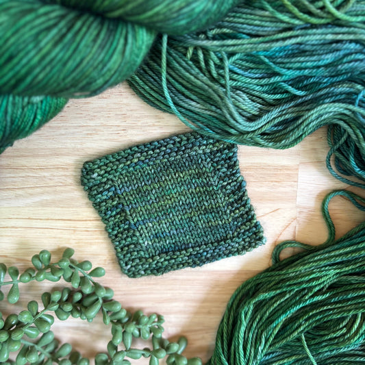 Green yarn skeins and a knitted swatch on a wooden surface