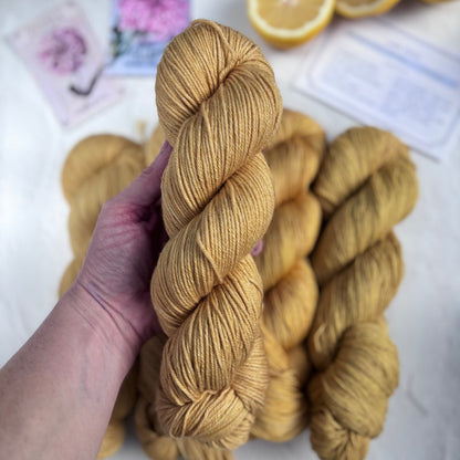 Hand holding skeins of yellow yarn with lemons and flowers in the background