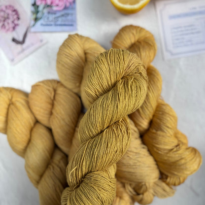Three skeins of yellow yarn on a white surface with a lemon and floral card in the background.