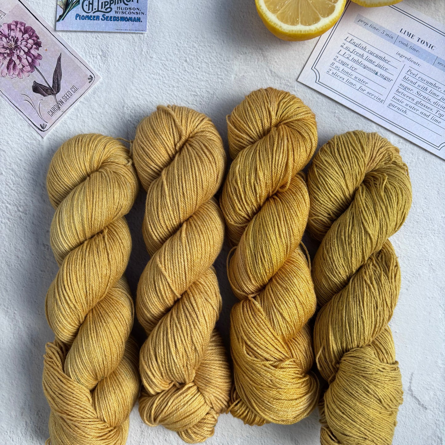 Four skeins of yellow yarn on a white surface with lemon halves and a card in the background.