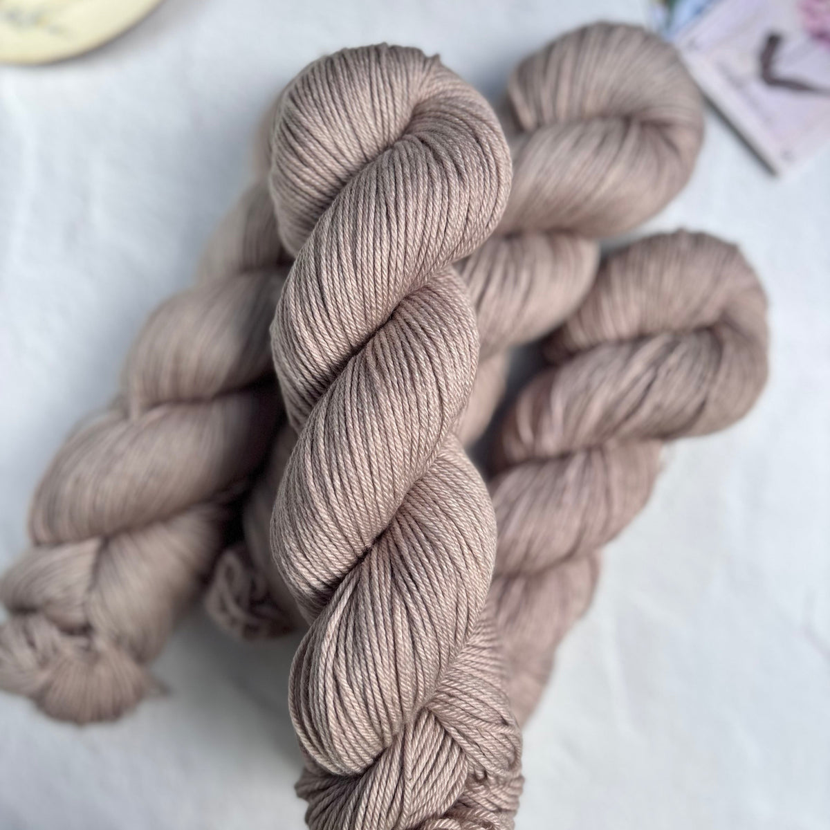 Skeins of beige yarn on a light surface with a cup and saucer in the background.
