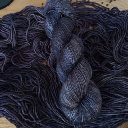 Charcoal gray skein of yarn on a wooden surface with other yarn and pumpkins.