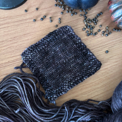 Knitted dark gray square with yarn and decorative elements on a wooden surface