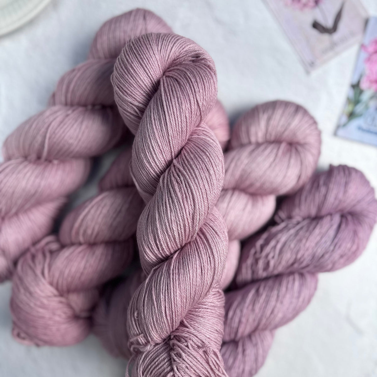 Skeins of pink yarn on a light surface with blurred floral decorations in the background