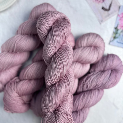 Skeins of pink yarn on a light surface with blurred floral decorations in the background