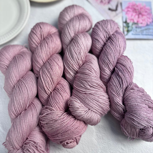 Three skeins of pink yarn on a white surface with a blurred background